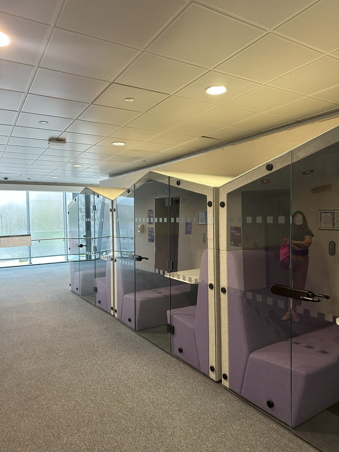 http://Corridor%20with%20enclosed%20meeting%20pods.%20The%20pods%20have%20glass%20doors%20inside%20you%20can%20see%20purple%20benches